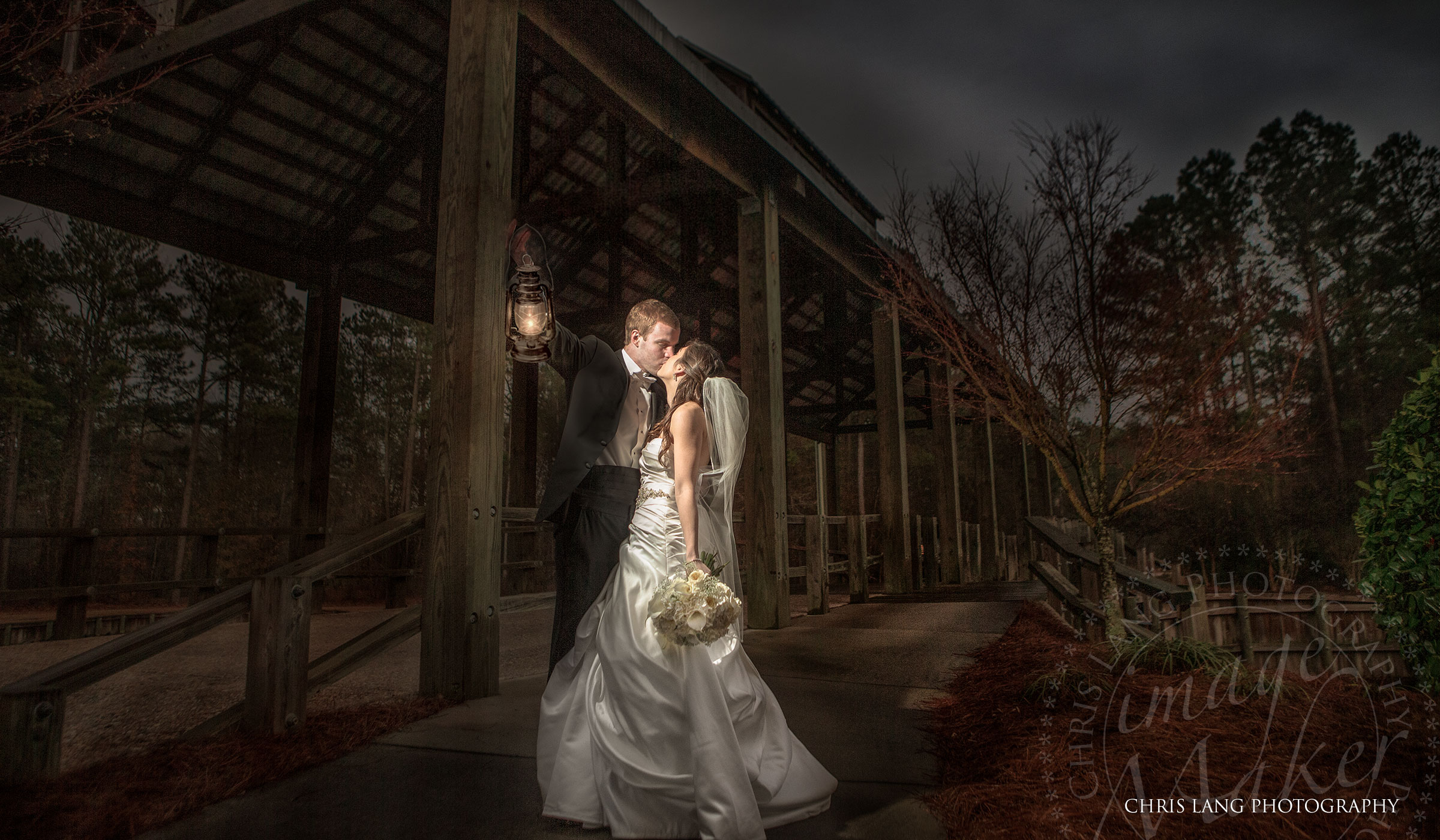 A creative wedding picture of a groom holding a lantern whilt kiissing his bride in her wedding dress. Wilmingotn NC Photographer