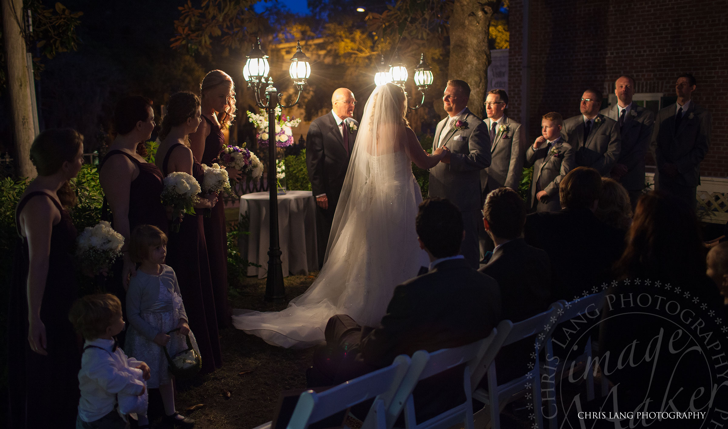 Bellamy Mansion Weddings - Wilmington NC Wedding Venue. photo of a bride and gromm at standing together holding hands during a wedding ceremony at the Bellamy Mansion at night. Wilmington NC Photographer